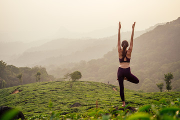 woman in violet cloth doing yoga on tea plantations in Munnar hill Kerala India