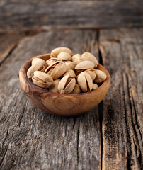 Pistachio nuts in  the wooden bowl  on a wooden background.