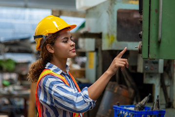 Young smart woman engineer in safety helmet working with electronic heavy industry machine in lathe...