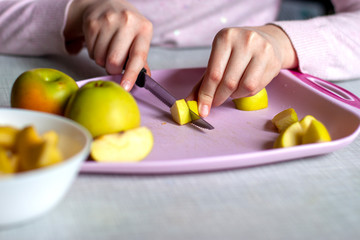 Healthy eating during quarantine. Green apples on a pink cutting board, which are cut into pieces by a knife women's hands.