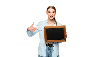 smiling pretty girl with braid pointing at empty chalkboard isolated on white