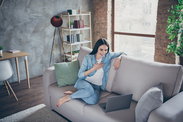 Full size photo of charming cute positive girl in good mood have covid-19 quarantine use laptop watch funny series laugh sit divan indoors in apartment