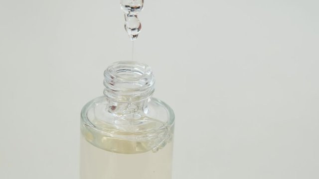 Women hand hold a glass bottle of iquid essential, collagen serum with dropper on blurred background, close up. White background