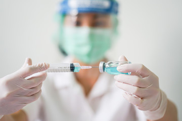 Close up medical doctor wearing face shield, medical mask and medical grove. She holding draw syringe and bottle with Coronavirus vaccine for 2019-nCoV COVID virus.