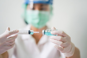 Close up medical doctor wearing face shield, medical mask and medical grove. She holding draw syringe and bottle with Coronavirus vaccine for 2019-nCoV COVID virus.