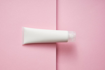 Top view of plastic tube with white cosmetic cream on pink background