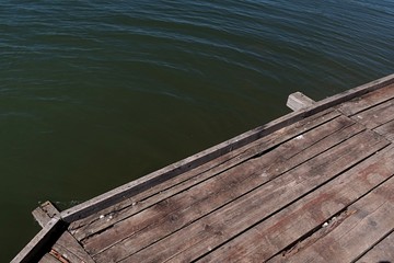 Detail of wooden molo pier with visible ends of support beams under surface boards.