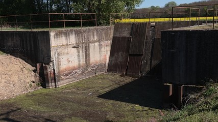Small river dam of sideway channel of Vah river, Slovakia with visible inflow part, grate for filtering dirt and dirty water. Spring season, rapeseed field in background. 