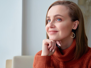 a positive girl in a brown jacket sits and dreams. a smile on her face. close up. copy space