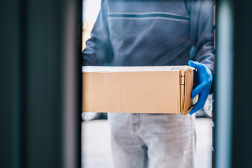 Deliverer leaving a package at the customer's door as a measure of protection against the coronavirus. Delivering a package to a house with blue latex gloves. Delivery man through the glass door.