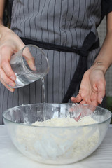The cook's hands knead the dough in a large glass bowl. Homemade cake. Housework.