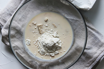 Flour, yeast and milk in a large glass bowl. Homemade cake. Concept of homework during the quarantine period.