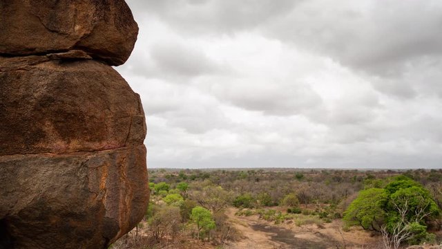 Slow linear timelapse of big granite rock boulders on overcast early morning showing texture, revealing African bush landscape in distance with green trees rainy clouds moving, start of summer season.