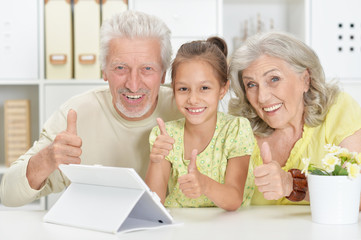 Portrait of grandparents with granddaughter using tablet