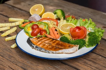 Grilled salmon steak on vintage wooden board with fork, olive oil, vegetables, herbs and spices on dark concrete background. Raw salmon fillet with vegetables, spices and lemon on wooden table.