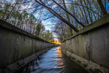 A stream in a concrete ditch or rainwater channel at night in forest. Storm drainage in the evening. The combination of nature and industry.