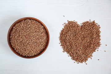 Buckwheat in a wooden bowl on a white table and next to a heart of buckwheat.