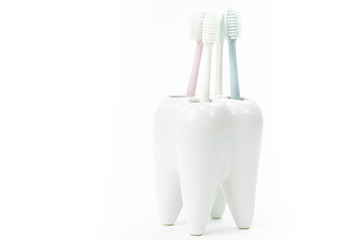 Fototapeta na wymiar toothbrush stand shaped like primary tooth with colorful toothbrushes pastel shades close up isolated on white background
