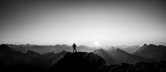 Man reaching summit enjoying freedom and looking towards mountains sunset. - obrazy, fototapety, plakaty