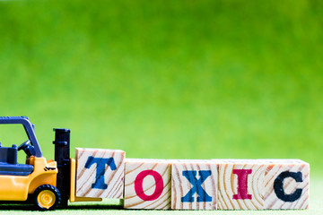 Toy forklift hold letter block t to fulfill word toxic on green background