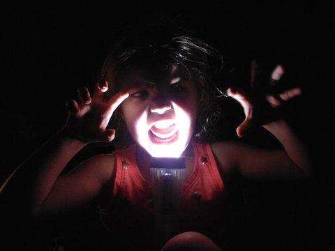 Girl With Illuminated Flashlight Making Face In Darkroom