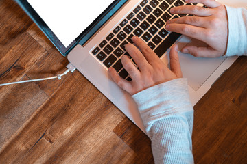 Hands pictured on the keyboard of a laptop typing something. 