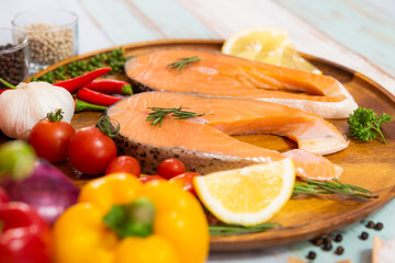 Fresh raw salmon steak with colorful vegetable and hot spice ingredient on wood plate in color wood plank background
