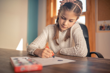 Beautiful 9 year old brunette girl painting on paper with pastel colors smiling