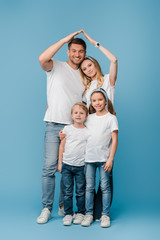 Fototapeta na wymiar happy family with kids making roof gesture over heads on blue