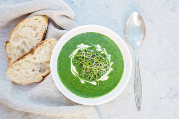 Cream soup of fresh spinach with cream and arugula microgreen in a white plate with ciabatta bread on a light gray background. Healthy and diet food. Flat lay.
