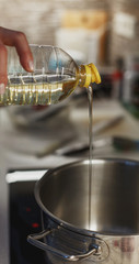 Close up of pouring vegetable oil into deep stainless steel pot