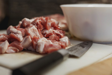 Pile of raw fresh sliced meat on a white plastic cutting board with knife and white bowl filled other ingredients