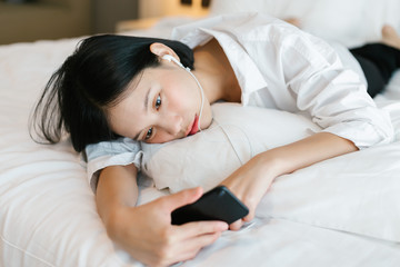 Beautiful asian female in white shirt calling mobile phone while working on bed. work from home concept.