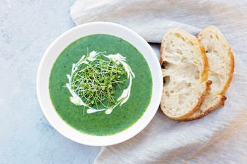 Cream soup of fresh spinach with cream and arugula microgreen in a white plate with ciabatta bread on a light gray background. Healthy and diet food. Flat lay.