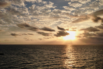 Naklejka premium Breathtaking sunset in the middle of the ocean, with yellow orange blue sky and white clouds, View from the deck of cruise ship. Travel vacation voyage landscape.