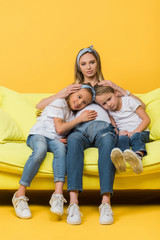 smiling pregnant mother hugging with happy daughter and son on sofa on yellow
