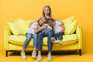 pregnant mother hugging with smiling daughter and son on sofa on yellow