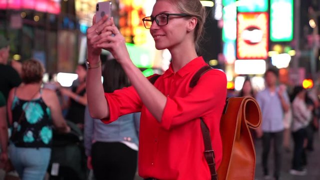 Happy hipster girl in red t-shirt and with stylish backpack using modern cellular for taking pictures while visiting metropolis, slow motion of good looking female traveler enjoying getaway journey
