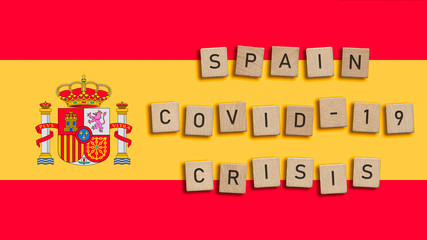 Spain Covid 19 crisis written with wooden tiles over Spanish flag background