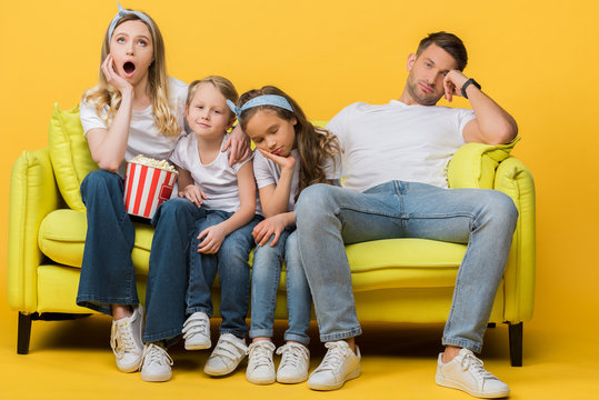 bored parents and kids watching movie on sofa with popcorn bucket on yellow