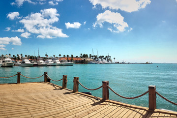 Aruba - Nov 16, 2016: Wooden pier at the bay with small yachts in Aruba. Sunny bay view with blue sky and white clouds. Dock of the bay.