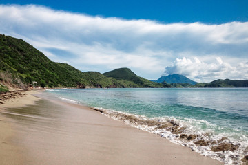 Fototapeta na wymiar St.Kitts Island/Saint Kitts and Nevis - Nov 29, 2016: Black sand beach view with mountains at the background. Beautiful travel picture.