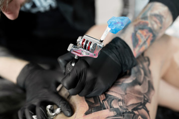 Close up image of the bearded tattoo male artist makes a tattoo on a female leg