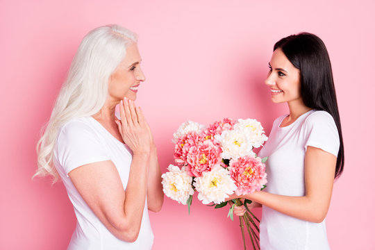 For You Mommy. Profile Photo Of Cheerful Aged Mother Young Daughter Ladies Spend Time Together Giving Fresh Flowers Bunch Wear White T-shirts Jeans Isolated Pastel Pink Color Background
