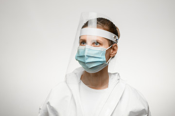 Fototapeta na wymiar young female nurse in medical mask and protective shield on her head looks away.