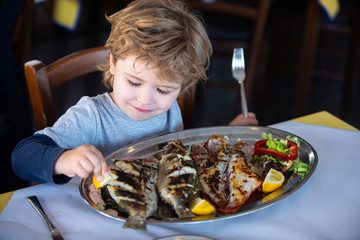 Fish for food. Child wuth lemon and fish plate meal. Dinner in sea restaurant. Seafood with iodine...