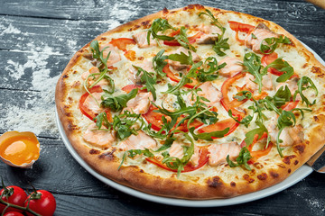 Baked pizza with salmon, tomatoes, melted cheese, white sauce and ruccola on a black wooden background in a composition with ingredients. Top view. Italian cuisine