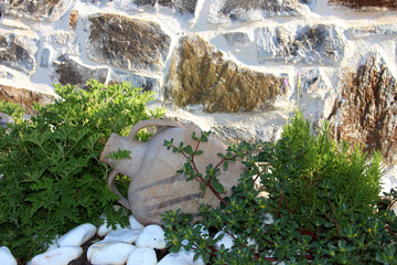 beautiful decor in the garden of wild plants, white pebbles and a clay jug on the background of a stone old wall