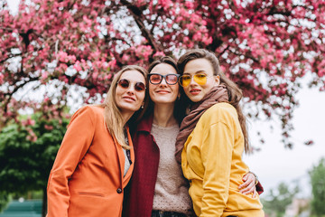 Best friends girls having fun, joy. Lifestyle. Beautiful young women in sunglasses dressed in the nice clothes smiling on a sunny day. photos of girls against the background of flowering trees