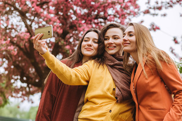Selfie - Three beautiful woman. Beautiful young women in sunglasses dressed in the bright clothes smiling on a sunny day. girls make photo of against the background of flowering trees